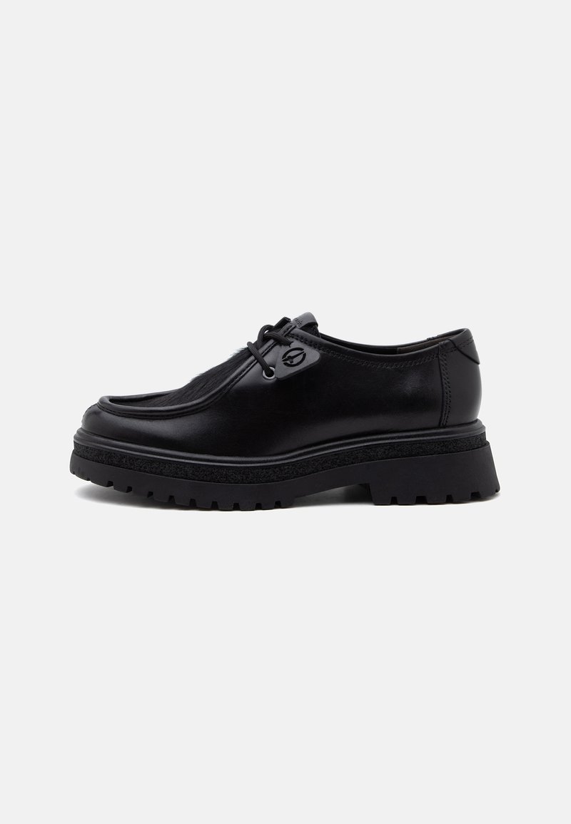 Chaussure noire en cuir à lacets avec une semelle épaisse texturée et un embout arrondi, vue de profil sur un fond gris clair uni.