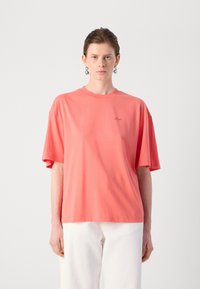 Coral oversized t-shirt made of soft cotton, featuring a round neckline, short sleeves, and small embroidered logo on the front.