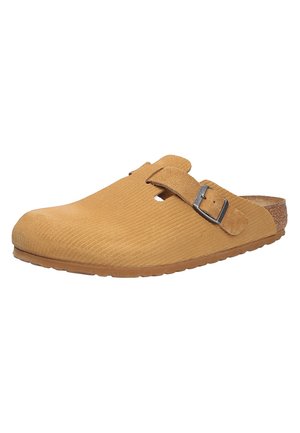 Beige Wildleder-Slipper mit gerippter Textur, verstellbarem Schnallenriemen und Korkfußbett. Abgerundete Zehenpartie und flexible Gummisohle.