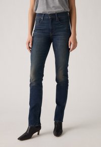 Μαύρες ψηλοκάβαλες τζιν παντελόνες σκούρου μπλε χρώματος με στενή εφαρμογή, ελαφριά ξεθώριασμα στους μηρούς, πέντε τσέπες και καθαρό στρίφωμα. Συνδυάζονται με μαύρες μπότες με τακούνι.