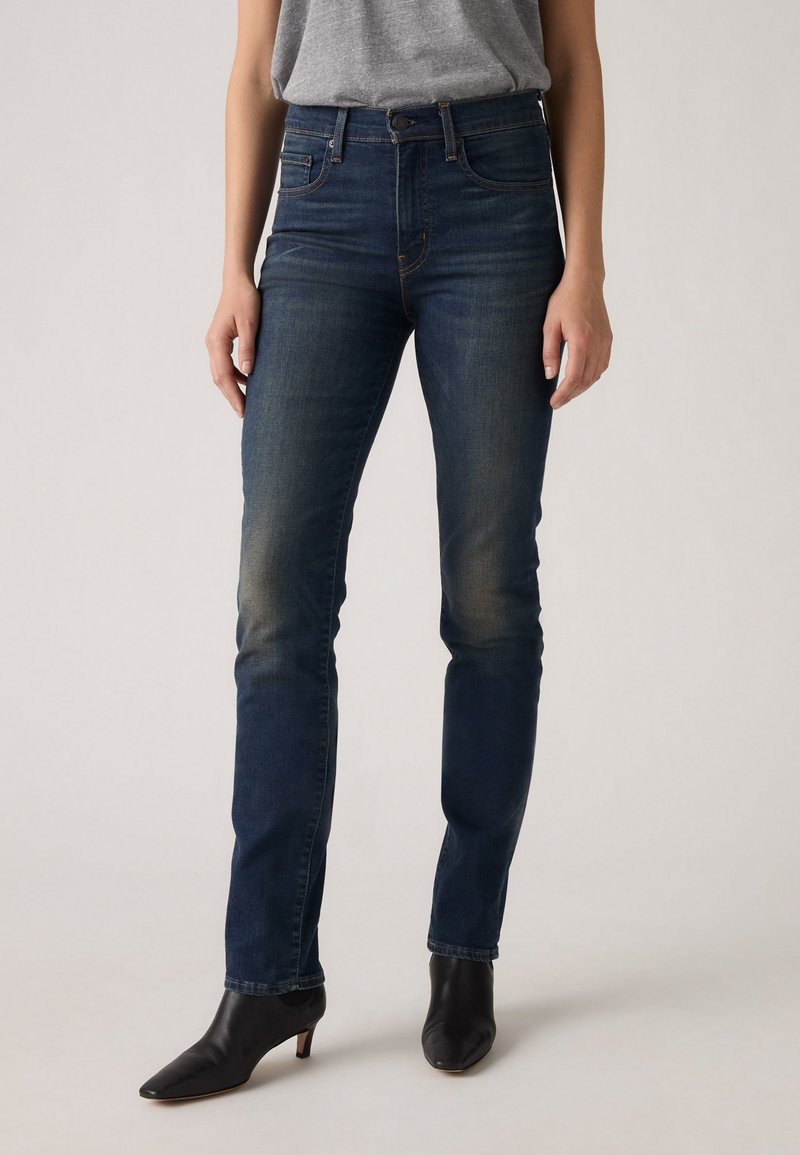 Μαύρες ψηλοκάβαλες τζιν παντελόνες �σκούρου μπλε χρώματος με στενή εφαρμογή, ελαφριά ξεθώριασμα στους μηρούς, πέντε τσέπες και καθαρό στρίφωμα. Συνδυάζονται με μαύρες μπότες με τακούνι.