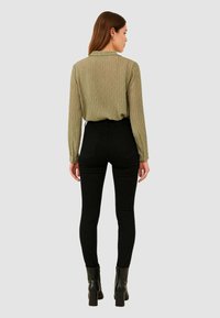 Blusa a maniche lunghe a coste verde oliva abbinata a jeans skinny neri a vita alta e stivaletti neri con tacco.