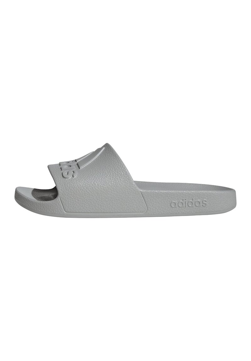 Graue, strukturierte Slidesandale mit erhabenem Logo, offener Zehenpartie und dezent geschwungenem Design, seitlich mit "adidas" gekennzeichnet.