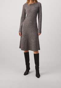 Robe à manches longues en tricot côtelé gris avec un corsage ajusté et une jupe évasée, associée à des bottes noires ajustées jusqu'aux genoux. Texture lisse.