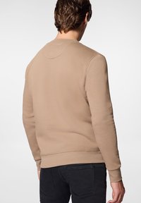 Beżowy sweter z okrągłym dekoltem wykonany z miękkiego materiału, z prążkowanymi mankietami i dolnym wykończeniem. Prosty design z dyskretnym logo przy dekolcie.