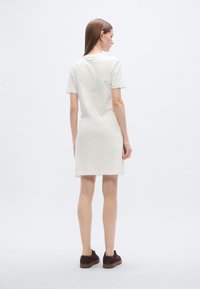 Λευκό φόρεμα με κοντά μανίκια, ίσια γραμμή, απαλό ύφασμα και πλαϊνές χαράξεις, σε συνδυασμό με καφέ δερμάτινα παπούτσια με κορδόνια. Στυλιζαρισμένο από πίσω.