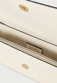 Ανοιχτό πορτοφόλι από κρεμ δέρμα, που δείχνει χρυσά κουμπώματα με κουμπί και εσωτερική ετικέτα με το όνομα της μάρκας "Tommy Hilfiger".