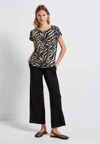 Svart och tan zebra-mönstrad topp med korta ärmar, tillsammans med svarta vida byxor och svarta mesh-skor utan snörning. Slät tygtextur.