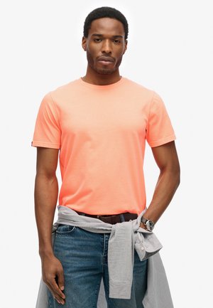 Neon-orange T-Shirt mit kurzen Ärmeln aus weichem Stoff, getragen mit blauen Jeans und einem gestreiften Hemd, das an der Taille gebunden ist.