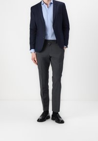 Granatowa marynarka na jasnoniebieskiej koszuli, zestawiona z szarymi spodniami i czarnymi butami. Marynarka posiada dwa guziki; spodnie mają wysoki fason.