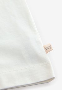 Világoskék pamut póló egyenes szegéllyel, a varrás közelében egy kis "Little Bird" címkével ellátott szövött címkével. Puha tapintású, minta nélküli.