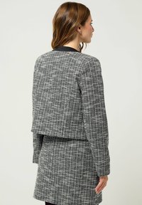 Giacca di tweed bianca e nera con un design corto, motivo testurizzato e colletto nero a tinta unita, dotata di maniche lunghe e taglio dritto.