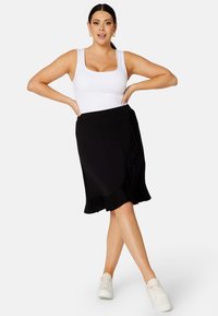 Gonna nera a tubino con orlo arricciato, abbinata a un top aderente bianco e sneakers bianchi. Tessuto liscio con una vita elasticizzata.