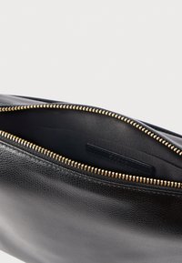 Plic negru din piele cu exterior texturat, fermoar auriu și interior neted cu etichetă de marcă.