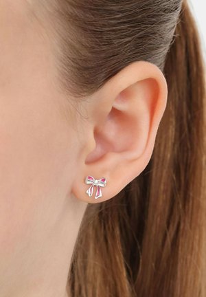 Orecchini a cerchio in argento a forma di fiocco con accenti di smalto rosa e un piccolo cristallo centrale, che mostrano una finitura liscia e lucida.