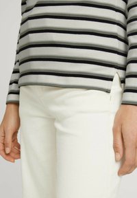 Randig långärmad skjorta i grå, svart och grön med rundad nederkant; matchas med vita byxor. Har sidslitsar och en mjuk textur.