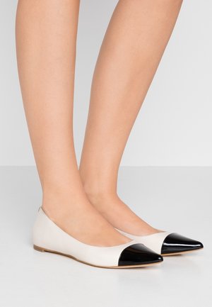 Ballet flats van beige leer met een glanzende zwarte punt. Vloeiende textuur, lage profiel en minimalistisch ontwerp.