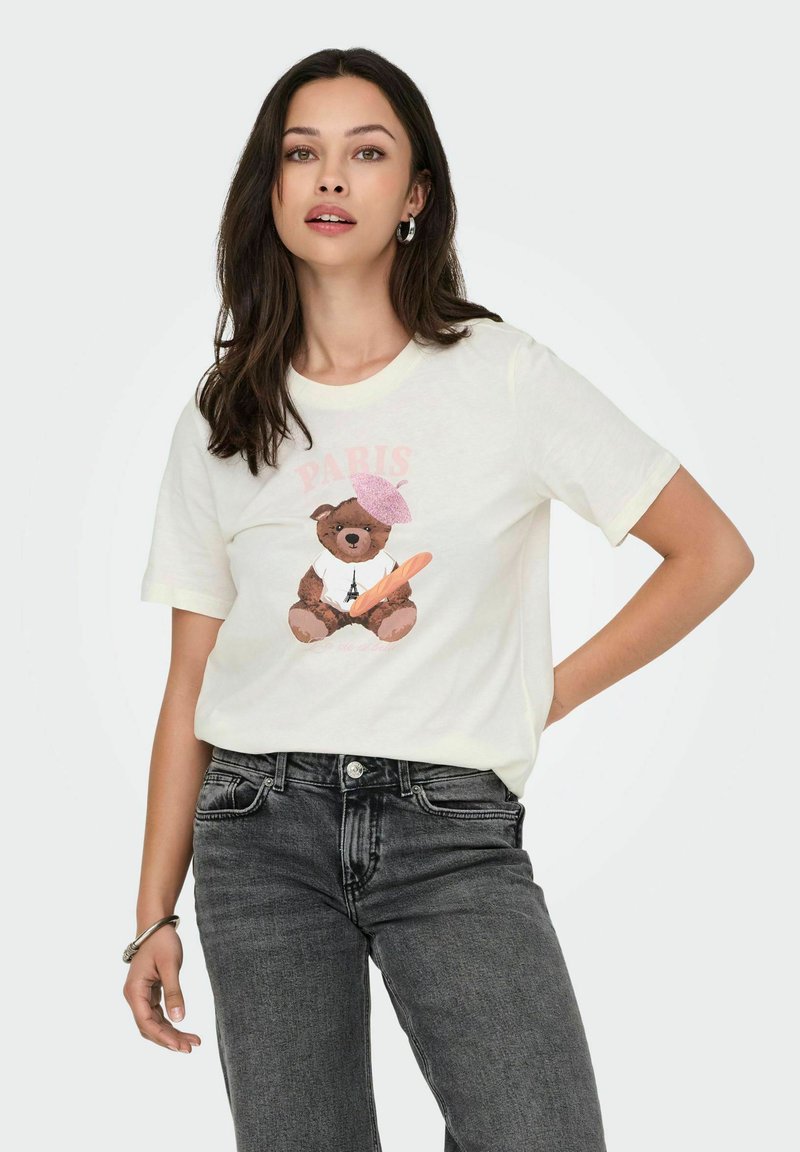 Hvid bomulds T-shirt med rund hals, der har et grafisk motiv af en brun bjørn iført en lyserød beret og holder en baguette, mod en lys baggrund.