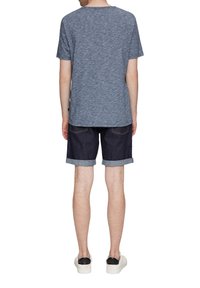 Niebieska heatherowa koszulka z krótkim rękawem, zestawiona z ciemnoniebieskimi szortami dżinsowymi z podwiniętymi mankietami. Na stopach białe trampki.