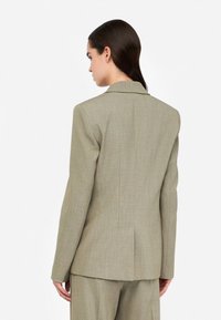 Blazer verde oliva chiaro con finitura texturizzata, ventaglio singolo sul retro e rever a punte, abbinato a pantaloni coordinati.