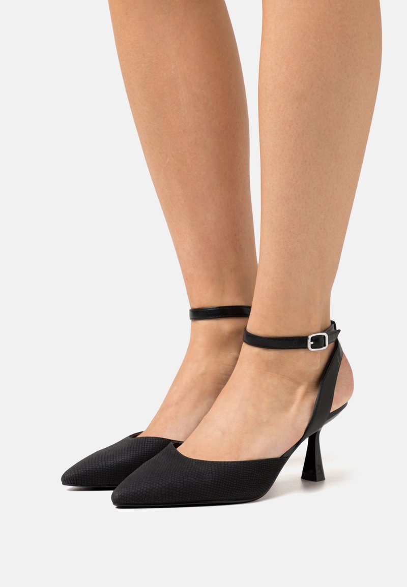 Chaussures à talons hauts noires avec un corps texturé, un bout pointu et une bride de cheville ornée d'une boucle argentée.