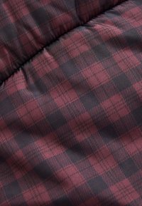 Tissu à carreaux bordeaux et noir avec une texture lisse, présentant un motif à carreaux régulier et un léger éclat, plié avec des coutures visibles.