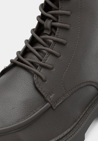 Mörkgrå läderstövel med en slät yta, platta snörningar, förstärkta öglor och en sydd söm längs sulan.