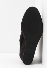Chaussure en daim noir avec une semelle plate, dotée d'un fond en caoutchouc texturé et de détails cousus. Nom de la marque "NEW LOOK" visible sur la semelle.
