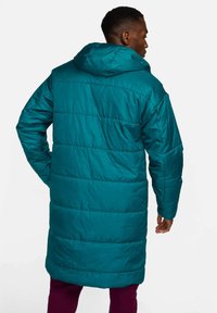 Geacă puffer teal cu glugă, având un design matlasat și mâneci lungi. Materialul are o textură netedă cu un finisaj lucios.