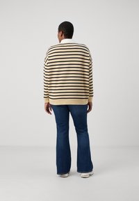 Randig tröja i krämfärg och svart, med en avslappnad passform, ribbade ärmslut och en vit krage, ihop med mörkblå utsvängda jeans.