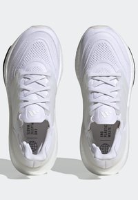 Paire de chaussures de sport blanches avec des lacets, une tige en mesh respirant et "END PLASTIC WASTE" imprimé à l'intérieur de chaque chaussure.