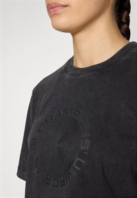 Black cotton t-shirt with a crew neck, featuring a textured circular logo and the word "CHAMPIONS'" in embossed lettering.