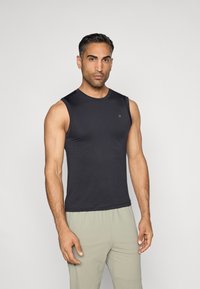 Melnā bez piedurknēm sporta krekls, kas izgatavots no gludas auduma. Pieder apaļš kakla izgriezums un mazs logo uz krūšu daļas. Pieguļošs dizains.