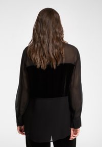 Czarna koszula wykonana z połączenia przezroczystych i aksamitnych tkanin, z długimi rękawami, prostym krojem oraz gładką fakturą z widocznymi przeszyciami.