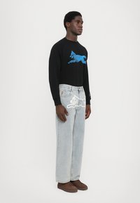 Black long-sleeve shirt with blue running dog graphic, paired with light blue loose-fit jeans featuring white cat and text accents, and brown sneakers.