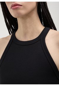 Gros plan sur une personne avec des cheveux tressés portant un haut sans manches noir à côtes, montrant le cou, les lèvres et les épaules.