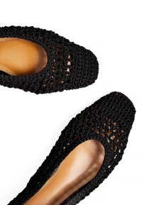 Ballerine nere intrecciate con punta arrotondata, caratterizzate da un design a taglio e un sottopiede beige liscio. La texture superiore è a maglia aperta, creando un aspetto traspirante.