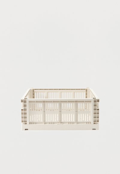Caisse de rangement empilable en plastique beige avec des fentes de ventilation, présentée vide sur un fond blanc uni.