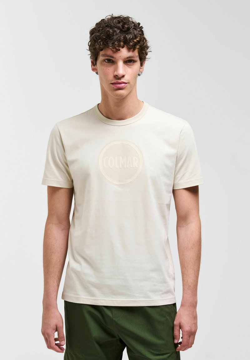 Hellbeiges T-Shirt aus Baumwolle mit rundem Ausschnitt und einem kreisförmigen "COLMAR"-Logo in etwas dunklerem Farbton in der Mitte.