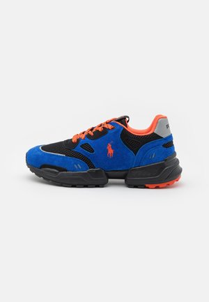 Zapatilla deportiva azul y negra con cordones y forro naranja, suela acolchada y un logo de jinete a caballo en el lateral, vista desde el lado exterior.