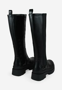 Botas altas de cuero negro con suelas robustas, cremallera lateral en una bota y panel elástico en la otra para un ajuste y comodidad óptimos.