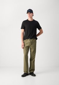 Black crew-neck t-shirt, olive green trousers, and black shoes. The hat is dark with a small blue logo. Straight leg design, minimal texture.