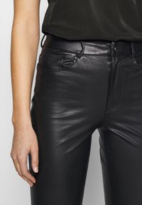 Svarta läderbyxor med en åtsittande design, slät yta och subtil sömnad. Har framfickor och en knappstängning.