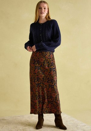 Marineblauer Strick-Cardigan mit Rundhalsausschnitt und Knopfverschluss, kombiniert mit einem langen, dunkelblumenbedruckten Rock und braunen Absatzstiefeln.