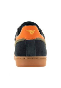 Scarpa da uomo sportiva con tomaia in suede nero, accentuata da un tacco in pelle arancione, logo dorato e suola in gomma marrone.