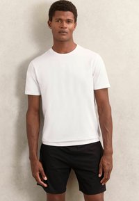 Tricou alb din bumbac, cu mâneci scurte, guler rotund, asortat cu pantaloni scurți negri. Design simplu, textură netedă, potrivit pentru ținute casual.