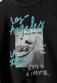 Fekete kapucnis pulóver, amelyen egy gördeszkás grafikai nyomtatás látható pálmafákkal, türkiz színű felirattal, amely a "Los Angeles" és a "SKATE IS A LIFESTYLE" szöveget tartalmazza.