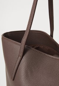 Brown leather tote bag featuring a textured surface, two top handles, and an open top design. Interior has a coordinating fabric lining.