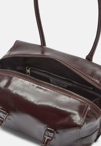 Ciemnobrązowa skórzana torba na ramię z podwójnymi uchwytami, z częściowo otwartym zamkiem błyskawicznym, ukazującym wewnętrzną kieszeń na zamek i metkę marki.