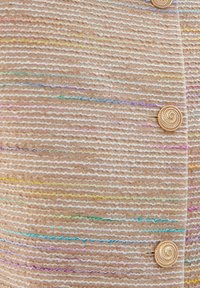 Texturovaná béžová tkanina se širokými vodorovnými pruhy s barevnými akcenty. Dva spirálové zlaté knoflíky na přední části dodávají designu zajímavost.